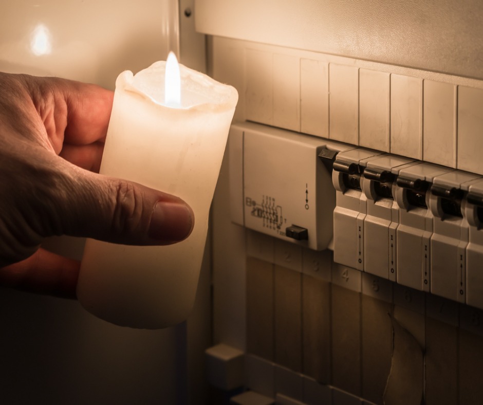 Photo of a hand holding a candle in front of a fusebox