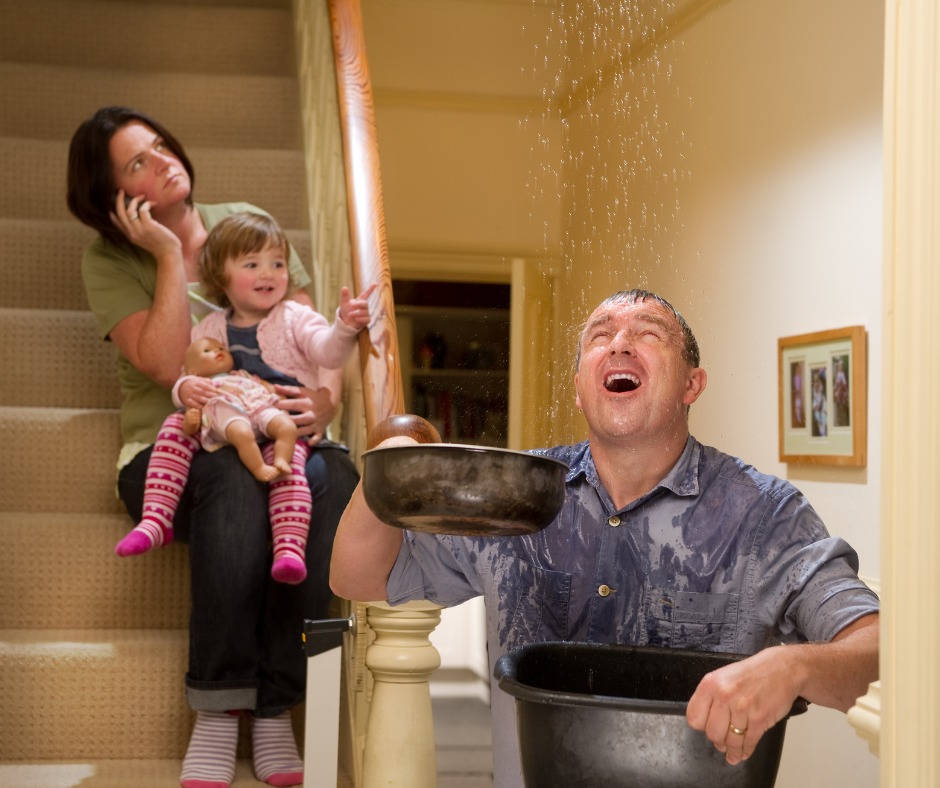 Photo of a man holding up buckets to catch water dripping from the ceiling. 