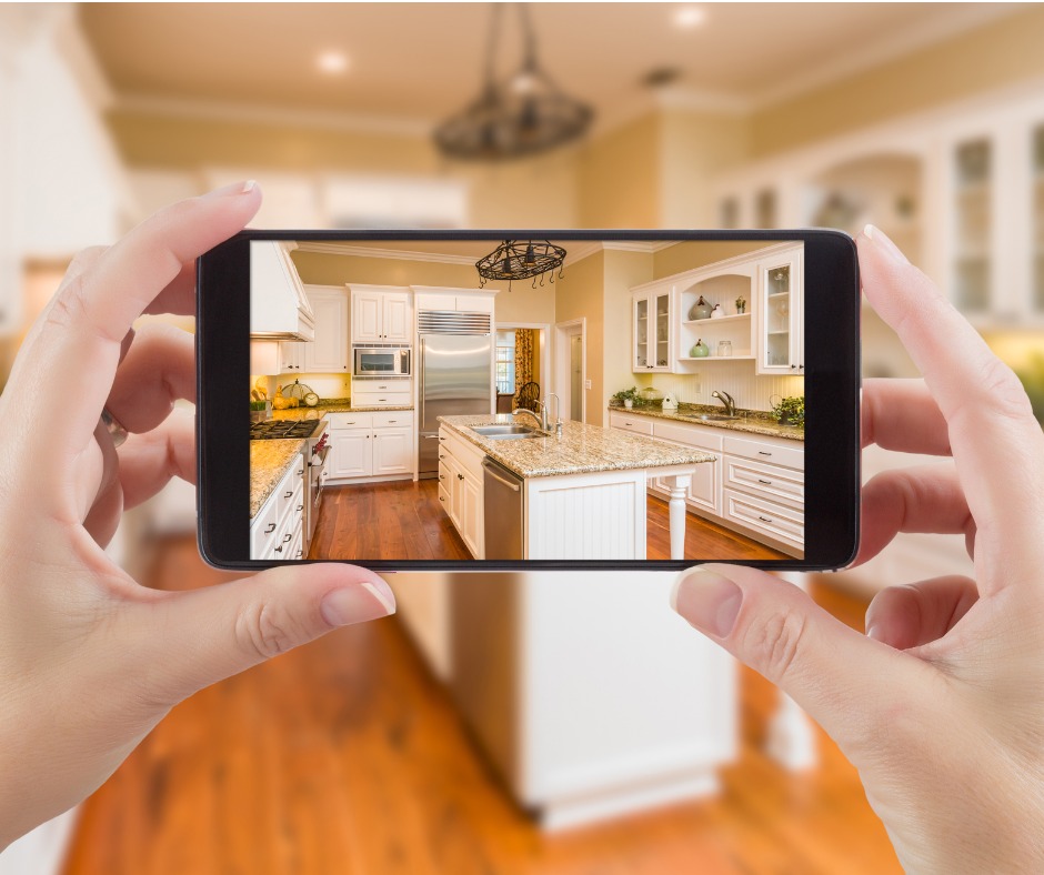 Photograph of a woman's hand's holding a mobile phone to photograph her kitchen.