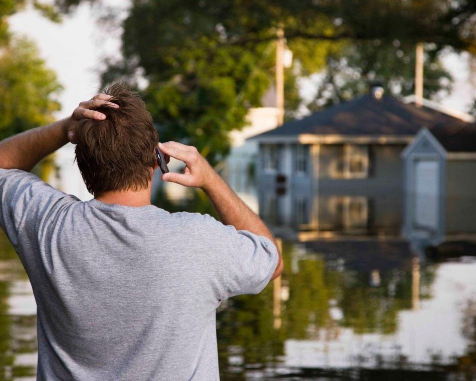 Man making a call with his hand on his head as he looks at his flooded home.