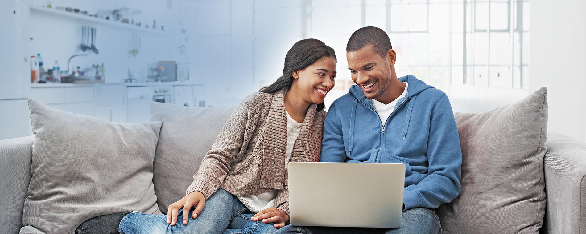 Couple sitting on a couch looking at a laptop.