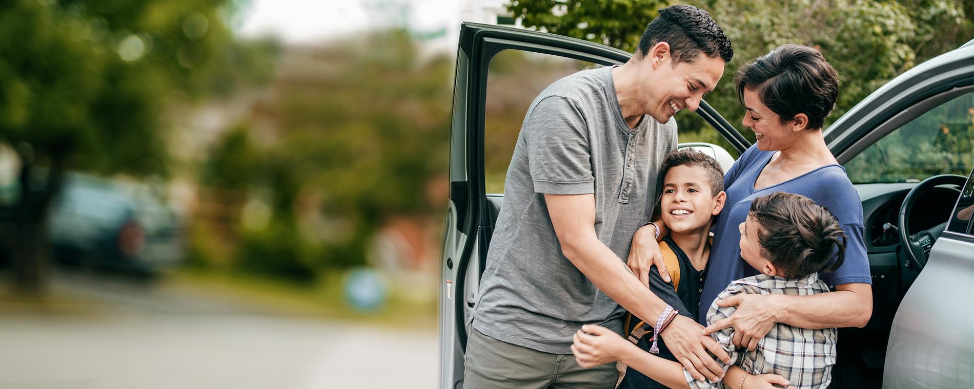 Photo of a family hugging next to a car
