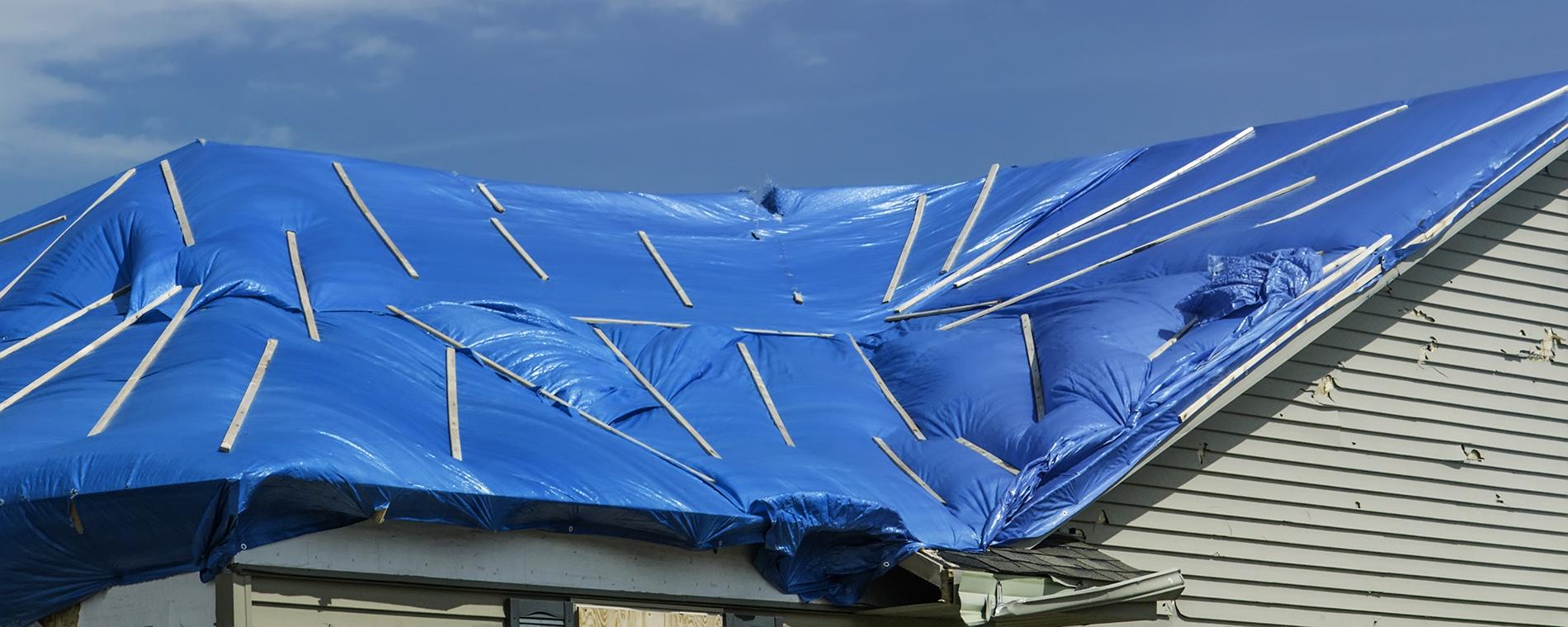 Photo of a damaged roof covered by a blue tarp.